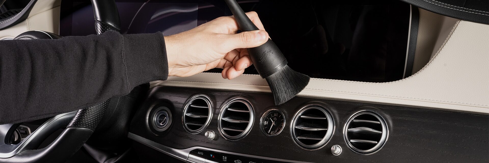 Een cardetailer is met een kwastje het interieur van de auto stofvrij aan het maken.