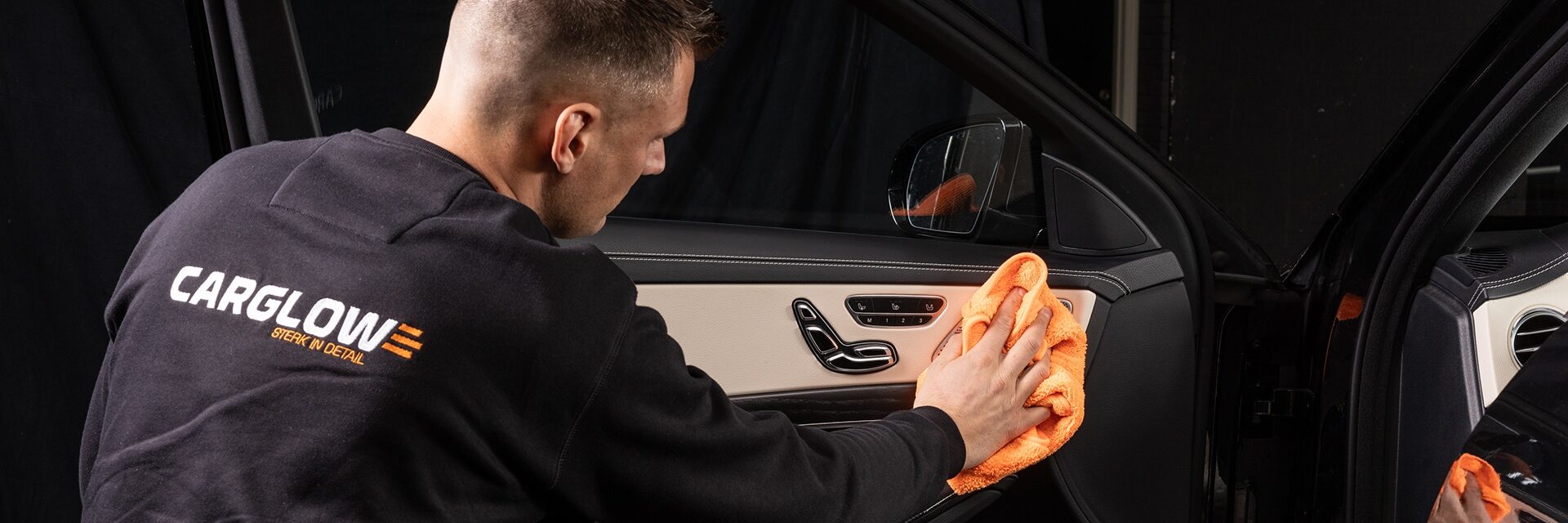 Een cardetailer is met een oranje microvezeldoek het interieur van de auto aan het reinigen.